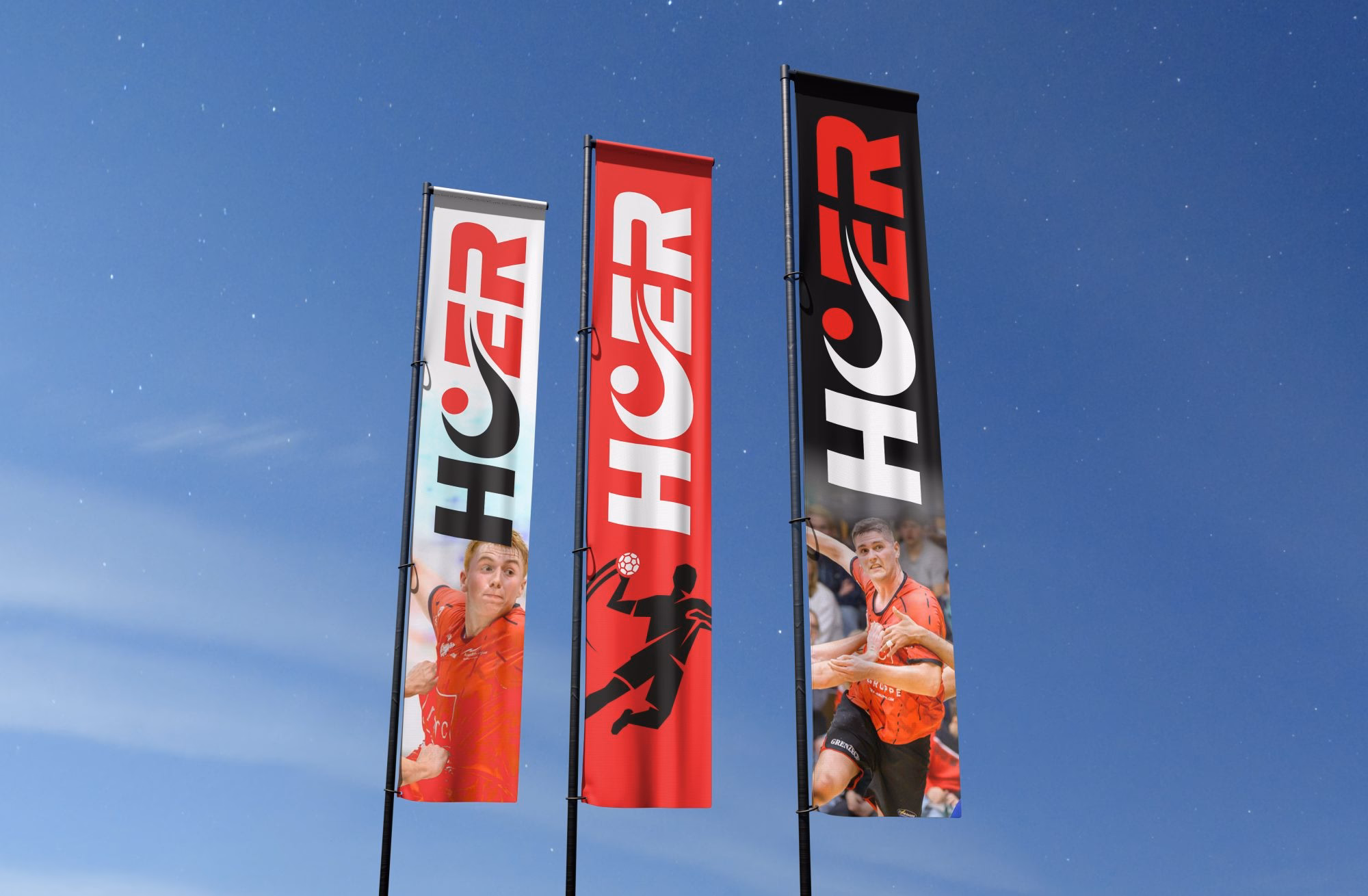 Drei Fahnen mit "HCER" Logo und Sportlern in roten Trikots gegen blauen Himmel.